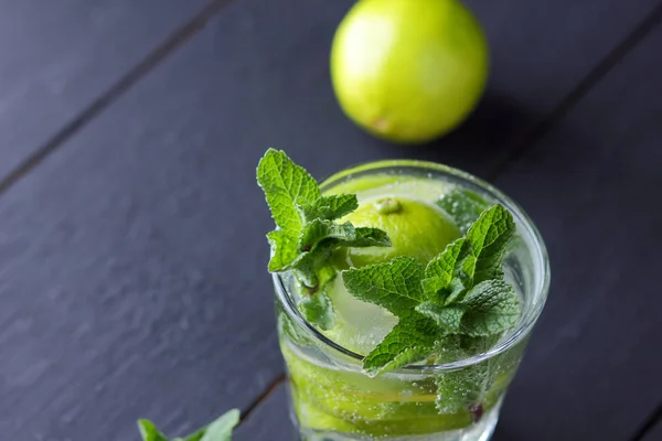 Minimalist cocktail, mojito on a dark background, summer cocktail with lime and mint, refreshing drink with lemon, fresh mint for cocktail, celebratory drink with ice, vegan, copy space, blank for designer, art