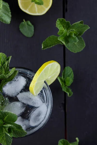 Mojito on a dark background, summer cocktail with lime and mint, refreshing drink with lemon, fresh mint for cocktail, celebratory drink with ice, copy space, minimalist cocktail, art