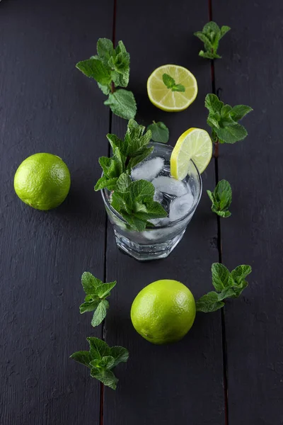 Mojito on a dark background, summer cocktail with lime and mint, refreshing drink with lemon, fresh mint for cocktail, celebratory drink with ice, copy space, minimalist cocktail, art