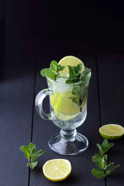 Mojito on a dark background, summer cocktail with lime and mint, refreshing drink with lemon, fresh mint for cocktail, minimalist cocktail, celebratory drink with ice, vegan, copy space, blank for designer