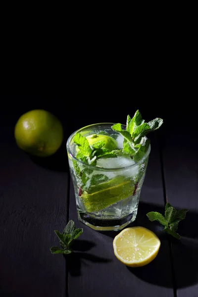 Mojito on a dark background, summer cocktail with lime and mint, refreshing drink with lemon, fresh mint for cocktail, minimalist cocktail, celebratory drink with ice, vegan, copy space, blank for designer