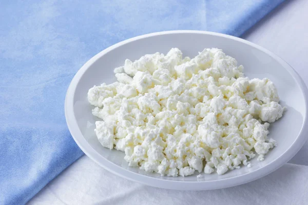 Cheese, fresh cottage cheese on a white plate, goat curd and blue napkin, dairy product on a light background, French breakfast, food, protein diet, healthy food, minimalism in food, health