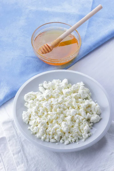 Cheese, fresh cottage cheese on a white plate, goat curd and blue napkin, honey on a light background, French breakfast, white soft cheese and honey, protein diet, healthy food, minimalism, health, pop art