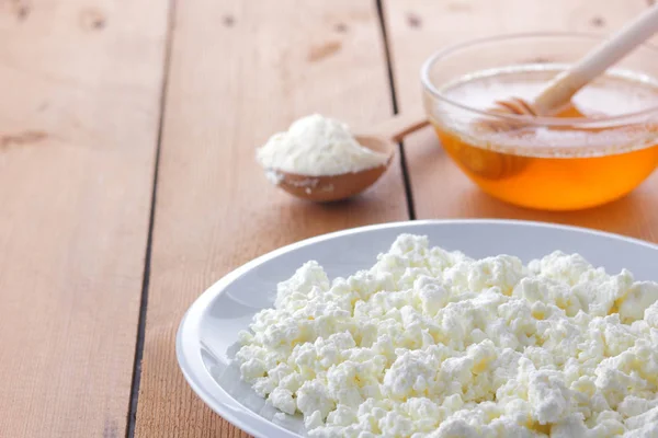 Cheese, fresh cottage cheese in a white plate, wooden spoon, cottage cheese and honey on a wooden background, sour cream in a wooden spoon, dairy products on a natural background, retro style, minimalism, French breakfast