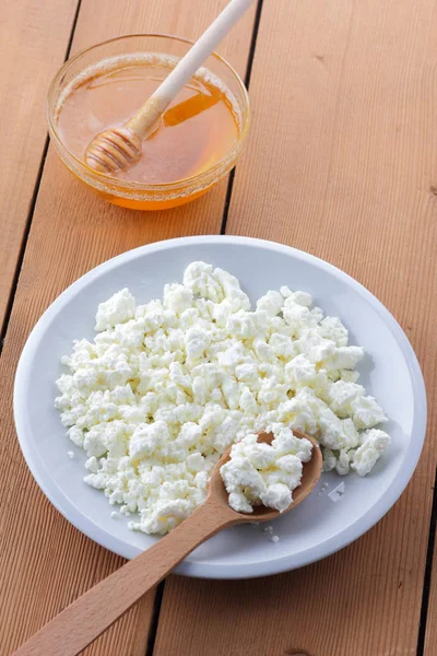 Cheese, fresh cottage cheese in a white plate, wooden spoon, cottage cheese and honey on a wooden background, sour cream in a wooden spoon, dairy products on a natural background, retro style, minimalism, French breakfast