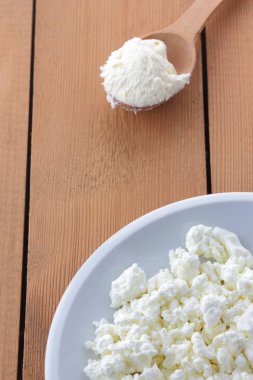 Peynir, taze peynir beyaz tabak, tahta kaşık, lor ahşap arka plan üzerinde ekşi krema bir tahta kaşık, doğal arka plan, retro tarzı, minimalizm, Fransız kahvaltı süt ürünleri