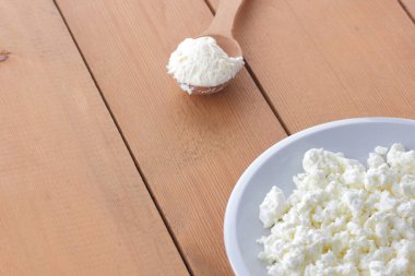 Peynir, taze peynir beyaz tabak, tahta kaşık, lor ahşap arka plan üzerinde ekşi krema bir tahta kaşık, doğal arka plan, retro tarzı, minimalizm, Fransız kahvaltı süt ürünleri