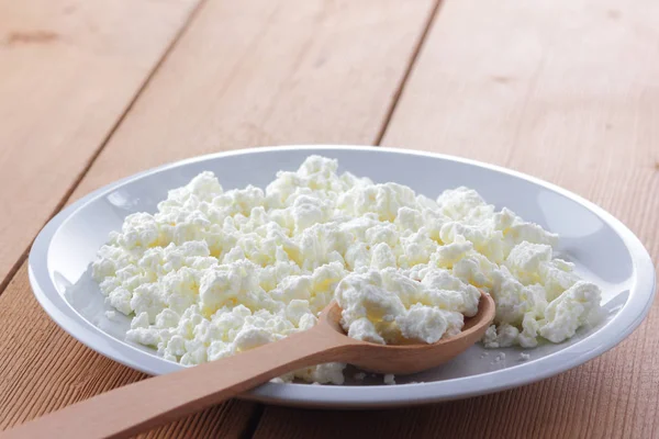 Cheese, fresh cottage cheese in a white plate, wooden spoon, curd on a wooden background, sour cream in a wooden spoon, dairy products on a natural background, retro style, minimalism, French breakfast