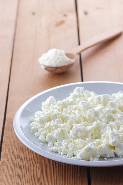 Cheese, fresh cottage cheese in a white plate, wooden spoon, curd on a wooden background, sour cream in a wooden spoon, dairy products on a natural background, retro style, minimalism, French breakfast