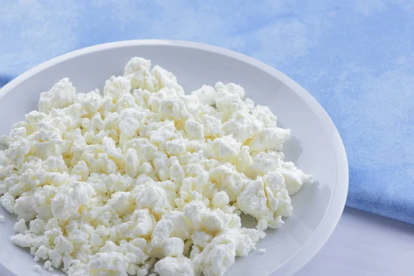 Cheese, fresh cottage cheese on a white plate, goat curd and blue napkin, dairy product on a light background, French breakfast, protein diet, healthy food, minimalism in food, health, art