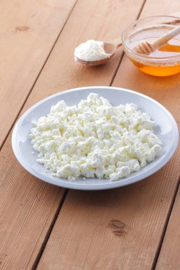 Peynir, taze peynir beyaz tabak, tahta kaşık, süzme peynir ve bal ahşap arka plan üzerinde içinde ekşi krema bir tahta kaşık, süt ve süt ürünleri doğal arka plan, retro tarzı, minimalizm, Fransız Kahvaltı, sanat