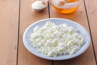 Peynir, taze peynir beyaz tabak, tahta kaşık, süzme peynir ve bal ahşap arka plan üzerinde içinde ekşi krema bir tahta kaşık, süt ve süt ürünleri doğal arka plan, retro tarzı, minimalizm, Fransız Kahvaltı, sanat