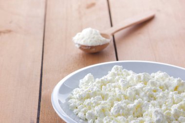 Ahşap arka plan, beyaz bir tabak, tahta kaşık, bir tahta kaşık ekşi krema, süt ve süt ürünleri doğal arka plan, rustik tarzı, minimalizm, Fransız Kahvaltı, sanat taze peynir peynir