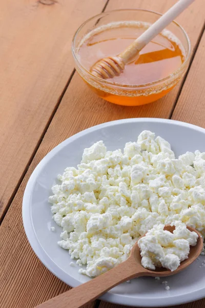 Peynir, taze peynir beyaz tabak, tahta kaşık, süzme peynir ve bal ahşap arka plan üzerinde içinde ekşi krema bir tahta kaşık, süt ve süt ürünleri doğal arka plan, retro tarzı, minimalizm, Fransız Kahvaltı, sanat