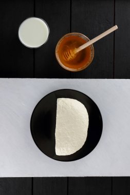 Peynir, peynir siyah bir plaka üzerinde ev yapımı peynir ve bal bir ahşap arka plan, minimalizm, ahşap çatal bıçak takımı, tatlım, bir bardak, kopya alanı, karanlık bir arka plan üzerine bir bardak süt kefir