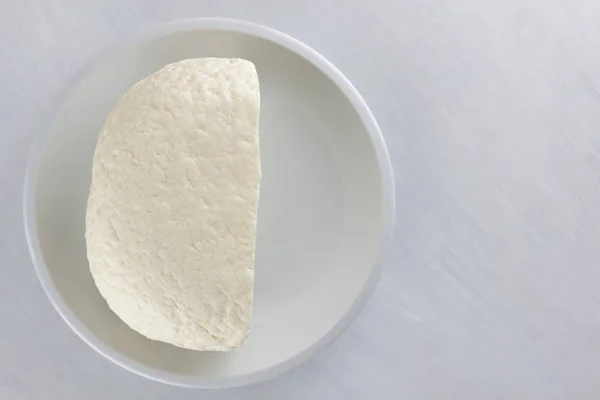 Cheese, soft cheese on a white plate, homemade cheese on a wooden table, black and white color, minimalism, Italian rustic cheese, copy space, dairy product on a wooden board, art