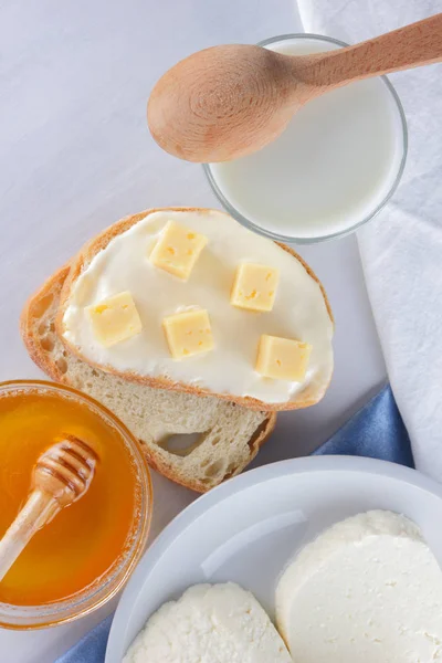 Cheese on a white plate, a glass of yogurt, a sandwich with soft cheese, minimalism, top view, copy space, a piece of bread with hard cheese, blue cloth, French breakfast, white cheese on a white background