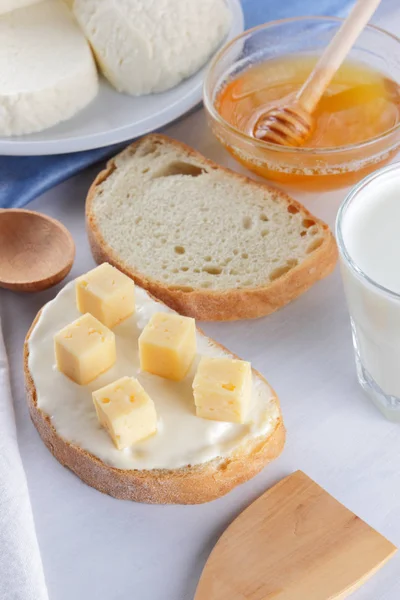 Cheese on a white plate, a glass of yogurt, a sandwich with soft cheese, minimalism, top view, copy space, a piece of bread with hard cheese, blue cloth, French breakfast, white cheese on a white background