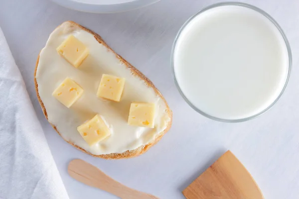 Cheese, dairy assortment on a white background, sandwich with soft cheese on a blue napkin, wooden background, wooden cutlery, top view, white cheese on a white plate, kefir in a glass, pop art