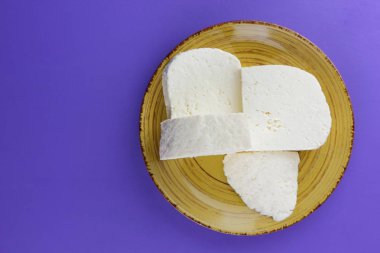 Peynir, bir mor arka plan, sarı bir plaka üzerinde beyaz peynir, süt ürünleri tarzında minimalizm, kopya alanı, üstten görünüm, süt Kahvaltı, tasarımcı, ultraviyole, sanat için boş bir Yunan peynir