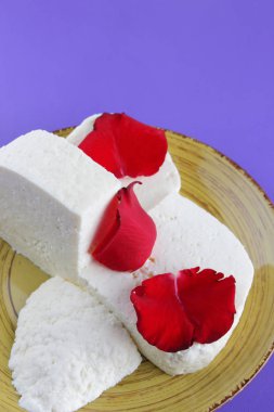 Peynir ve yaprakları kırmızı gül, mor bir arka plan üzerinde Yunan peynir, beyaz peynir süt ürünleri tarzında bir minimalizm, sarı bir tabakta kopyalama alanı, Festival gıda, süt Kahvaltı, ultraviyole