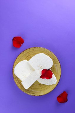 Peynir ve yaprakları kırmızı gül, mor bir arka plan üzerinde Yunan peynir, beyaz peynir süt ürünleri tarzında bir minimalizm, sarı bir tabakta kopyalama alanı, Festival gıda, süt Kahvaltı, ultraviyole