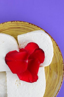 Peynir ve yaprakları kırmızı gül, mor bir arka plan üzerinde Yunan peynir, beyaz peynir süt ürünleri tarzında bir minimalizm, sarı bir tabakta kopyalama alanı, Festival gıda, süt Kahvaltı, ultraviyole