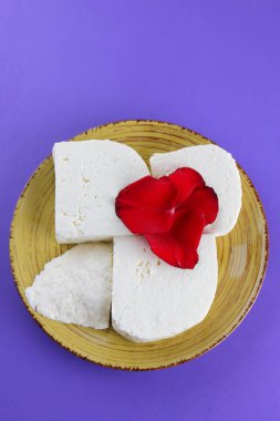 Peynir ve yaprakları kırmızı gül, mor bir arka plan üzerinde Yunan peynir, beyaz peynir süt ürünleri tarzında bir minimalizm, sarı bir tabakta kopyalama alanı, Festival gıda, süt Kahvaltı, ultraviyole