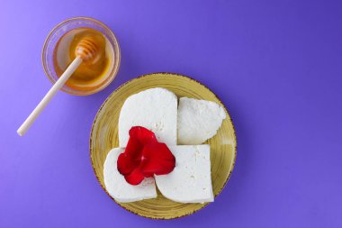 Peynir ve bal, yaprakları kırmızı gül, Yunan peynir bir mor arka plan, sarı bir plaka üzerinde beyaz peynir, minimalizm, tarzında süt ürünleri kopyalama alanı, Festival gıda, süt Kahvaltı, ultraviyole, tatlım