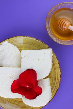 Peynir ve bal, yaprakları kırmızı gül, Yunan peynir bir mor arka plan, sarı bir plaka üzerinde beyaz peynir, minimalizm, tarzında süt ürünleri kopyalama alanı, Festival gıda, süt Kahvaltı, ultraviyole, tatlım