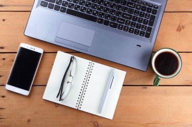 Bir dizüstü bilgisayar ve bir fincan kahve ahşap arka plan üzerinde bir iş istasyonu üzerinde eski bir Resepsiyon, bir smartphone ve bir defter, kalem ve gözlük işyeri, alan bir kopyasını, minimalist tarzı tasarımcı bir iş istasyonu
