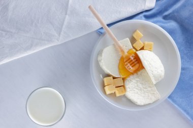 Peynir, süt ürün yelpazesine beyaz arka plan, beyaz peynir ve bal bir mavi peçete, ahşap arka plan, tatlım, üstten görünüm, peynir beyaz plaka üzerinde bir bardak kefir için tahta sopa üzerinde