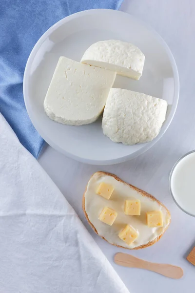 チーズ 白い背景に酪農品揃え 青いナプキン 木製の背景 木製カトラリー 白い皿の上の白いチーズ ガラス アートでケフィアの柔らかいチーズのサンドイッチ — ストック写真