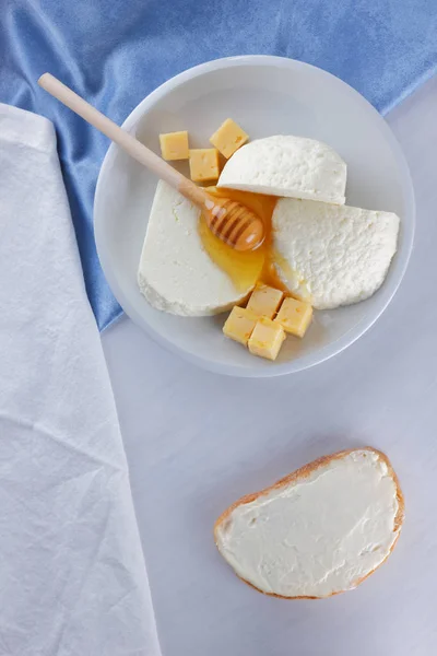 チーズ 白の背景 白チーズ 青ナプキン 木製の背景 平面図 白い皿にチーズ ケフィア ガラスの木製の棒の上に蜂蜜ミルク品揃え — ストック写真