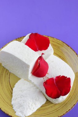 Peynir ve yaprakları kırmızı gül, mor bir arka plan üzerinde Yunan peynir, beyaz peynir süt ürünleri tarzında bir minimalizm, sarı bir tabakta kopyalama alanı, Festival gıda, süt Kahvaltı, ultraviyole, sanat