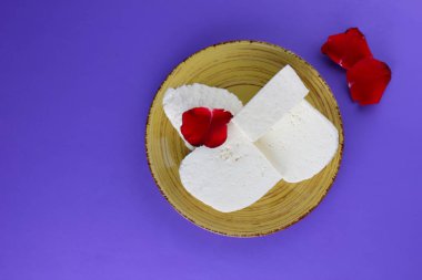 Peynir ve yaprakları kırmızı gül, mor bir arka plan üzerinde Yunan peynir, beyaz peynir süt ürünleri tarzında bir minimalizm, sarı bir tabakta kopyalama alanı, Festival gıda, süt Kahvaltı, ultraviyole, sanat