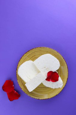 Peynir ve yaprakları kırmızı gül, mor bir arka plan üzerinde Yunan peynir, beyaz peynir süt ürünleri tarzında bir minimalizm, sarı bir tabakta kopyalama alanı, Festival gıda, süt Kahvaltı, ultraviyole, sanat