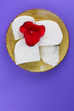 Peynir ve yaprakları kırmızı gül, mor bir arka plan üzerinde Yunan peynir, beyaz peynir süt ürünleri tarzında bir minimalizm, sarı bir tabakta kopyalama alanı, Festival gıda, süt Kahvaltı, ultraviyole, sanat