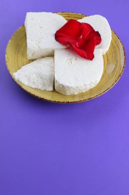 Peynir ve yaprakları kırmızı gül, mor bir arka plan üzerinde Yunan peynir, beyaz peynir süt ürünleri tarzında bir minimalizm, sarı bir tabakta kopyalama alanı, Festival gıda, süt Kahvaltı, ultraviyole, sanat