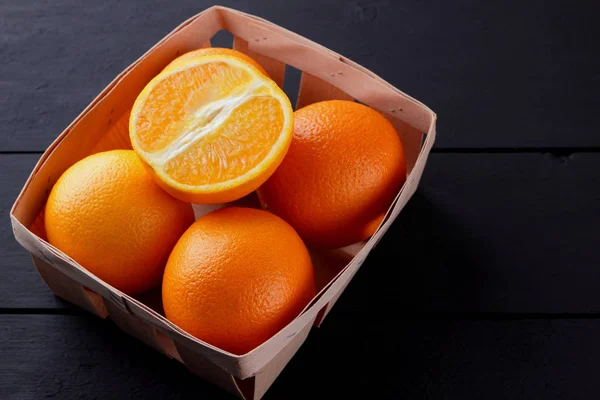 Oranges in a wooden box on a black background, citrus in retro style, copy space, orange fruits on a wooden background, tropical fruits in a box on a table, half orange for a vegan
