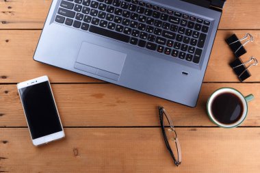 Kahve ahşap arka plan üzerinde eski bir Resepsiyon, smartphone ve bir dizüstü bilgisayar, iş istasyonunda bir dizüstü bilgisayar ve kalem ve işyeri, tasarımcı iş istasyonu, office gözlük