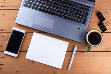 Kahve ahşap arka plan üzerinde eski bir Resepsiyon, smartphone ve bir dizüstü bilgisayar, iş istasyonunda bir dizüstü bilgisayar ve kalem ve işyeri, tasarımcı iş istasyonu, office gözlük