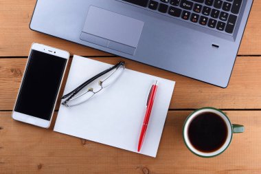 Kahve ahşap arka plan üzerinde eski bir Resepsiyon, smartphone ve bir dizüstü bilgisayar, iş istasyonunda bir dizüstü bilgisayar ve kalem ve işyeri, tasarımcı iş istasyonu, office gözlük