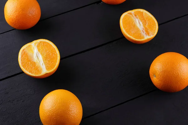 Whole and chopped oranges on a black background, citrus in retro style, copy space, a lot of oranges on a wooden background, a circle of tropical fruits on the table, fruits in the style of minimalism