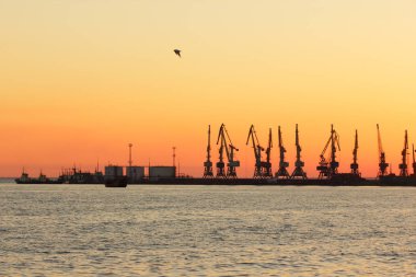 Seaport gün batımında, Vinç ufukta turuncu gökyüzü deniz ufuk, yatay, yüksek katlı Vinçler, deniz bir Dalgakıran inşaatı karşı limanda