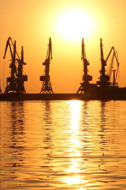 Seaport gün batımında, Vinç ufukta turuncu gökyüzü deniz ufuk, yatay, yüksek katlı Vinçler, deniz bir Dalgakıran inşaatı karşı limanda