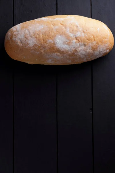 Round bread on a black background, bread from a stove on dark boards, a dough for a designer, copy space, rustic style, minimalism, top view, bakery