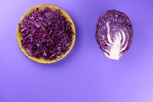 Chopped cabbage on a violet background, red cabbage on a yellow plate, copy space, top view, vegetarian food, fresh vegetables for salad, ultraviolet background, minimalism