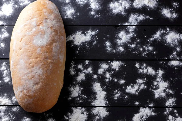 Bread with flour on a black background, wheat bread from a stove on dark boards, dough for a designer, copy space, rustic style, flour on a black background, top view, cooking