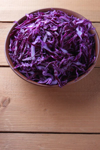 Chopped purple cabbage on a wooden background, red cabbage in a clay bowl, copy space, rustic style, vegetarian food, half fresh cabbage, minimalism